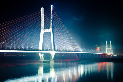 Illuminated bridge over river against sky at night