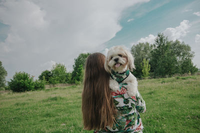 A girl with long hair carrying little dog shih tzu in her arms