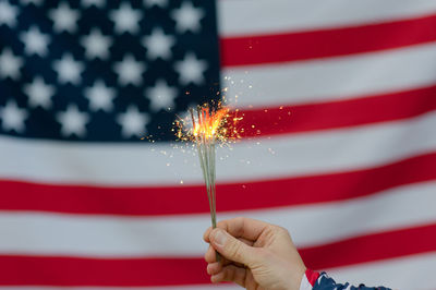 Cropped hand of person holding illuminated sparklers against american flag