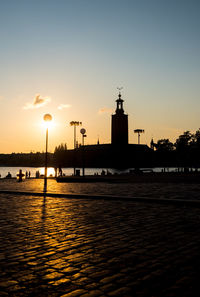 Street by silhouette city against sky during sunset