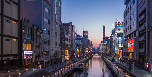 Illuminated street amidst buildings against sky at dusk