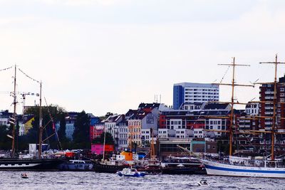 Sailboats moored on river by buildings against sky