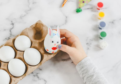 Hands of a  girl in a gray turtleneck laying an easter bunny egg with stickers in a cardboard box