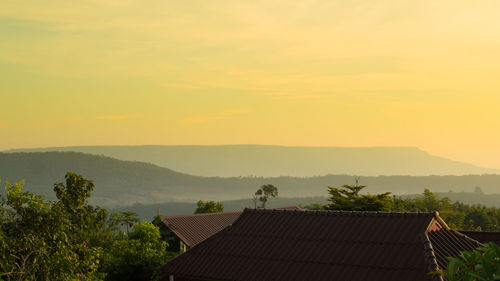 High section of houses amidst trees against sky during sunset