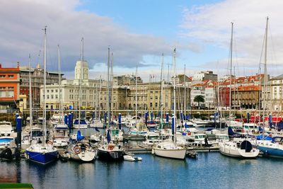 Sailboats moored at harbor against sky in city