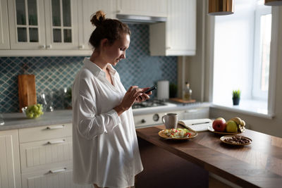 Businesswoman browsing smartphone during breakfast