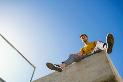 Low angle view of man sitting against blue sky