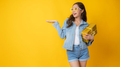 Portrait of young woman wearing sunglasses standing against yellow background