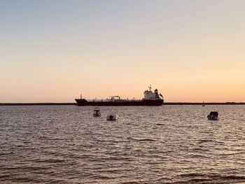 Ship sailing in sea against clear sky during sunset