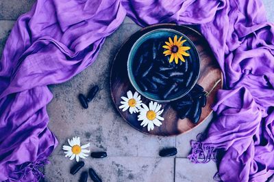 High angle view of grapes and daisies in bowl on plate by purple sheet