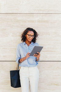 Young woman using digital tablet while standing on wall