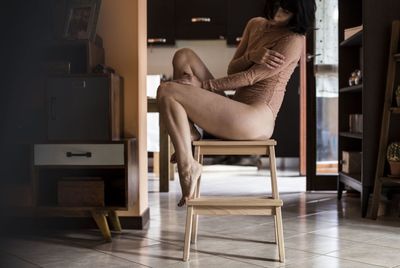Low section of seductive young woman sitting on stool at home