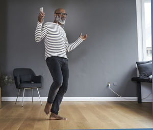 Mature man dancing alone at home, holding smart phone