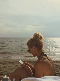 Woman using smart phone at beach against sky