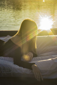 Young woman lies on a mattress on the water and the sunset reflects off the water with rays of light