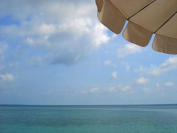 Cropped image of parasol by sea against sky