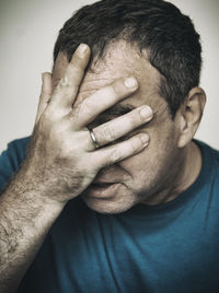 Close-up of man covering face with hand against white background