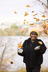 Smiling young woman throwing autumn leaves