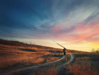 Old man silhouette walking a country road carrying dry tree branches on his shoulders