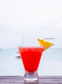Red drink in glass on table against sea