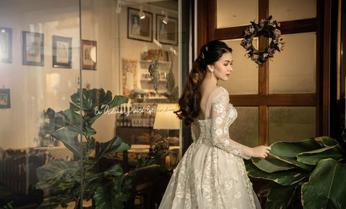 Woman wearing wedding dress while standing glass door