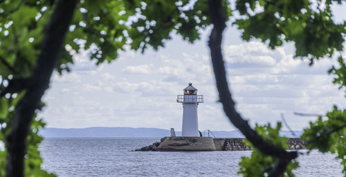 Lighthouse amidst trees and buildings against sky