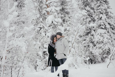 Beautiful young european couple in a sweater in winter in the forest hugging, kissing. 