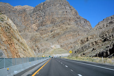 Empty road by mountains against clear sky