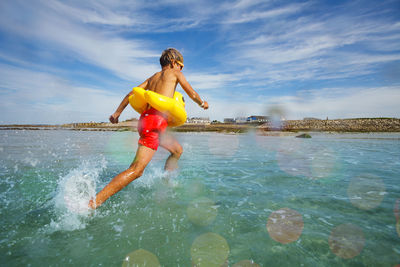 Rear view of woman jumping in sea against sky