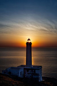 Lighthouse by sea against sky at dawn