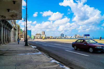 Vehicles on road amidst buildings in city against sky