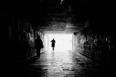 Rear view of silhouette man walking on footpath in tunnel