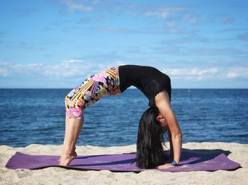 Full length of woman practicing wheel pose on beach