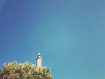 Low angle view of lighthouse by building against clear blue sky