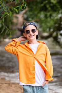 A boy in an orange shirt on the seashore. a child in sunglasses person
