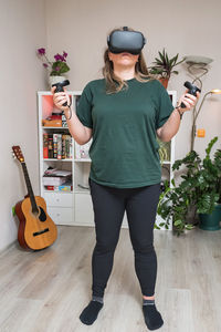 A girl in virtual reality glasses with joysticks in her hands stands in a room