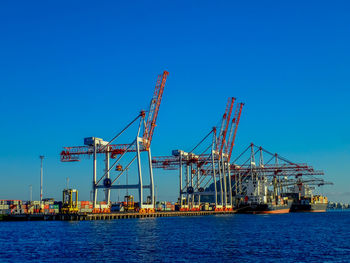 Cranes at commercial dock against clear blue sky