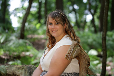 Portrait of young woman sitting on log in forest