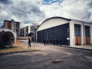 People walking on road by buildings against sky