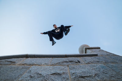 Low angle view of young man jumping from building against clear sky