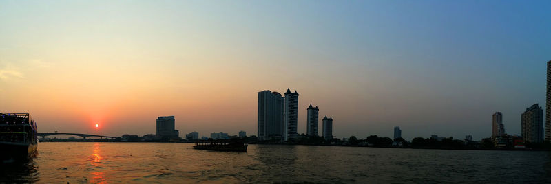 Modern buildings by sea against sky during sunset