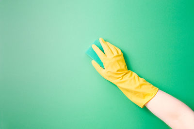A female hand in a yellow rubber glove washes a plain surface with a green paralon sponge