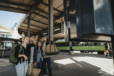 Woman showing arrival departure board to family while standing at railroad station