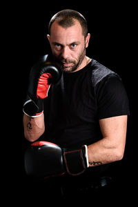 Portrait of mid adult man wearing boxing gloves against black background