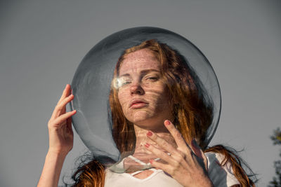 Close-up of woman wearing glass container while standing against gray background