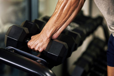 Midsection of man lifting dumbbell in gym