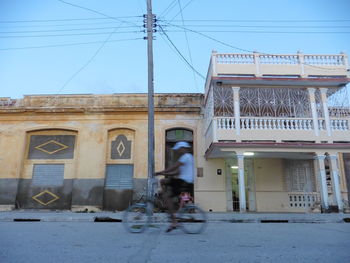 Man riding bicycle in city against clear sky