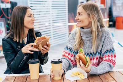 Two middle-aged women eat burgers at a street food truck fair.