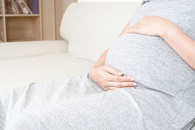 Midsection of pregnant woman sitting on sofa 