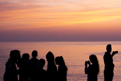 Silhouette people on beach against sky during sunset